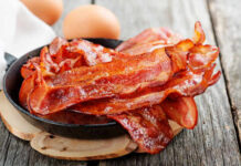 BACON DIET BACKFIRE – Heart Risk Skyrockets Crispy bacon strips in a cast iron skillet with eggs in the background
