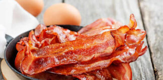 Crispy bacon strips in a cast iron skillet with eggs in the background
