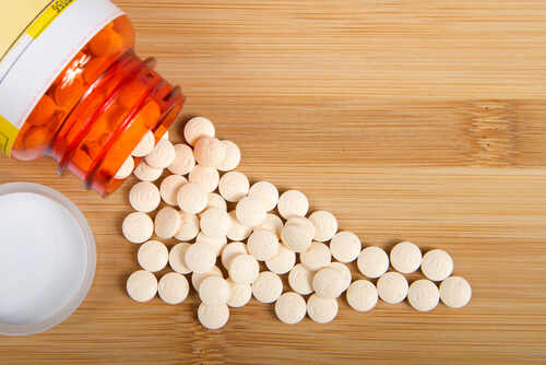 shutterstock_1717945684 (1).jpg Spilled white pills from a prescription bottle on a wooden surface