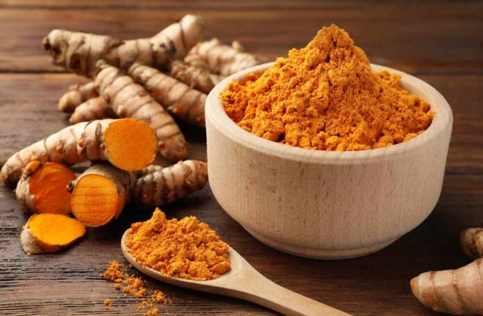 Turmeric powder in a wooden bowl with fresh turmeric roots