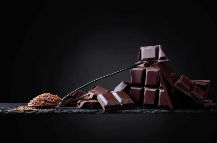 A pile of dark chocolate bars with cocoa powder on a black surface