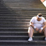 Synthetics vs. Cotton: The Workout Showdown An exhausted man in sportswear sitting on outdoor stairs, looking down.