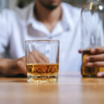 Alcohol’s Hidden Midlife Punch A man holding a whiskey glass and a bottle in a bar setting