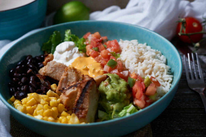 shutterstock_1887155650.jpg A vibrant bowl filled with grilled chicken, rice, black beans, corn, guacamole, and fresh vegetables