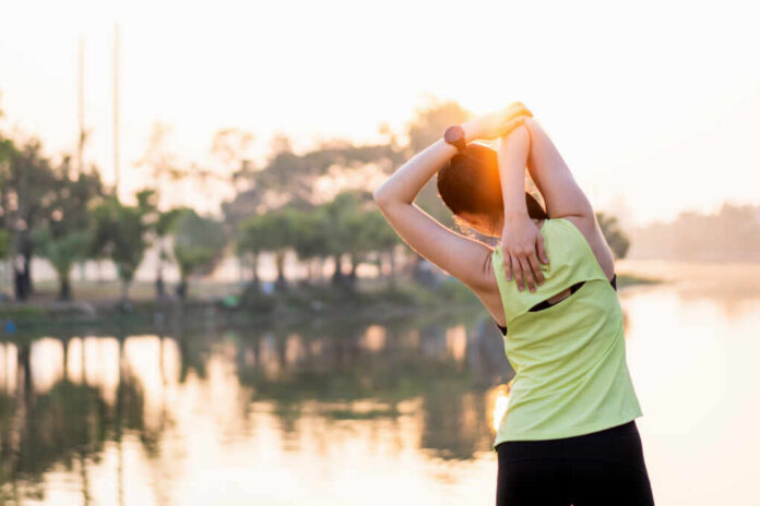 shutterstock_1922925317.jpg A woman stretching her arms by a lake during sunrise