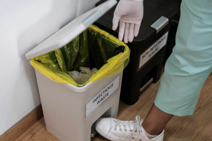shutterstock_2006524778.jpg Person in gloves disposing of waste in an infectious waste bin