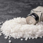 A glass salt shaker tipped over with salt spilling out