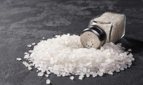 A glass salt shaker tipped over with salt spilling out