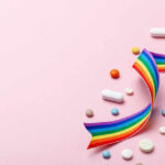 Colorful pills and a rainbow ribbon on a pink background