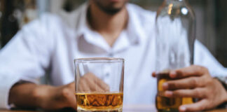 A man holding a whiskey glass and a bottle in a bar setting