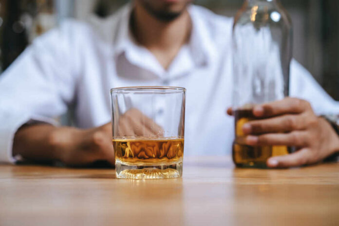 A man holding a whiskey glass and a bottle in a bar setting