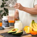 Person preparing a protein shake with fruits and whey protein powder in a kitchen