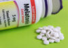 Bottle of melatonin tablets with some pills spilled on a green surface