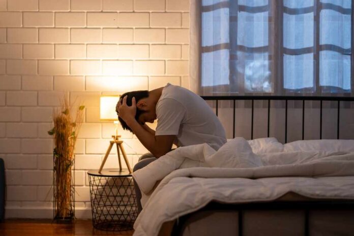 A person sitting on a bed with their head in their hands, expressing distress