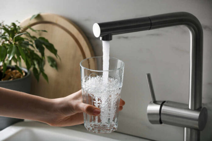 shutterstock2247078069jpg A hand holding a glass under a kitchen faucet pouring water