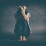 Looksmaxxing: When “Self‑Improvement” Hurts Instead of Helps A person sitting on the floor with their arms wrapped around their knees, conveying a sense of distress