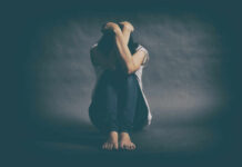Looksmaxxing: When “Self‑Improvement” Hurts Instead of Helps A person sitting on the floor with their arms wrapped around their knees, conveying a sense of distress