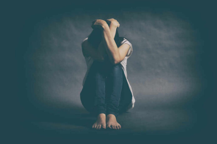 Teenager,Girl,With,Depression,Sitting,Alone,On,The,Floor,In A person sitting on the floor with their arms wrapped around their knees, conveying a sense of distress