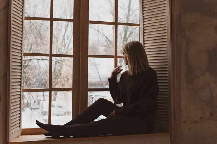 shutterstock_1240617826 Person sitting on a windowsill looking outside