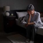 Older adult sitting on bed with head in hand