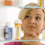 How to PREVENT UTIs Without Using Drugs A woman thoughtfully looking at a medicine cabinet filled with various medications