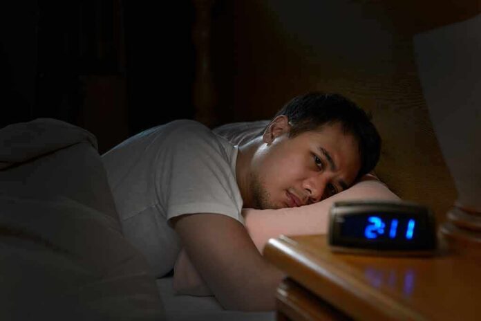 shutterstock_662022817 Man lying awake in bed watching an alarm clock