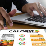 Processed Protein in Diet – Weak Muscle Warning! Person using a calorie counter app on a tablet while working on a laptop