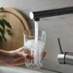 A hand holding a glass under a kitchen faucet pouring water