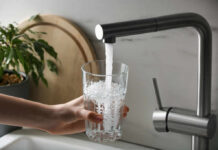 A hand holding a glass under a kitchen faucet pouring water