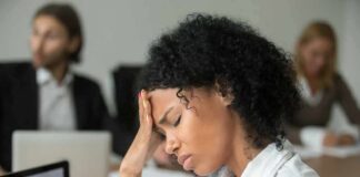 Woman in office holding her head with eyes closed