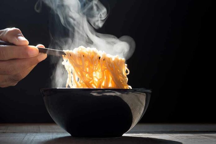 shutterstock_1034426287 Steaming noodles lifted from a black bowl with chopsticks