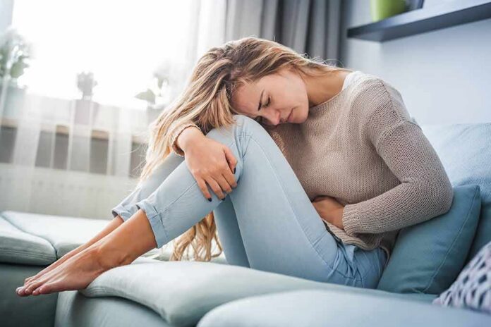 shutterstock_1254094441 Woman holding her stomach in pain on a sofa