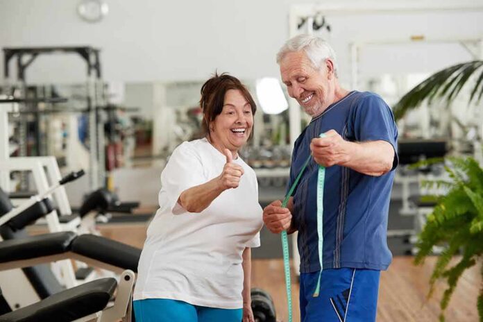 shutterstock_1395947015 Older couple in gym smiling and holding a measuring tape