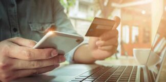 Hands using smartphone and credit card beside a laptop