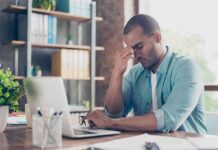 Digital Burnout: How to Reset an Overstimulated Brain Man at desk pinching bridge of nose beside laptop