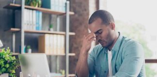 Man at desk pinching bridge of nose beside laptop