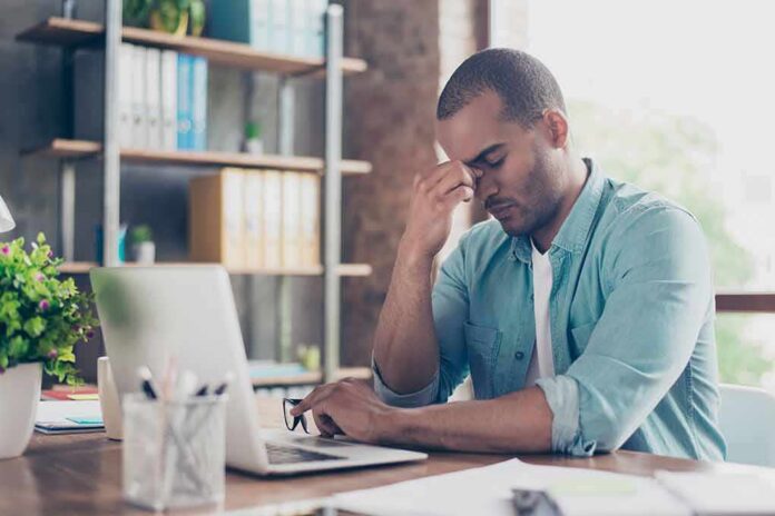 shutterstock_735692464 Man at desk pinching bridge of nose beside laptop