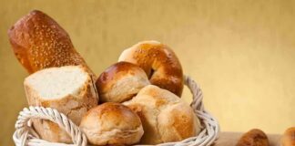 A basket filled with various types of fresh bread and rolls against a golden background