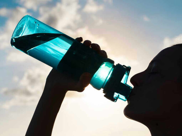 Silhouette of person drinking from a water bottle.