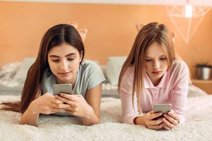 Two girls lying on a bed using smartphones