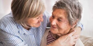 Two older women share a warm embrace on a couch