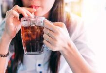 Soda And Booze Spike Gout Risk person sipping iced drink from a glass mug with a straw