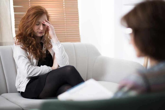 shutterstock_1077356072 Woman with hand on forehead sitting on couch during counseling session