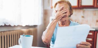Older woman covering her face while reading a document at a kitchen table