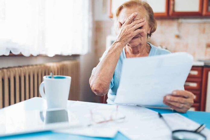 Older woman covering her face while reading a document at a kitchen table