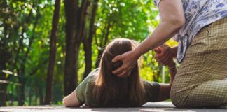 Person assisting someone lying on a path in a park