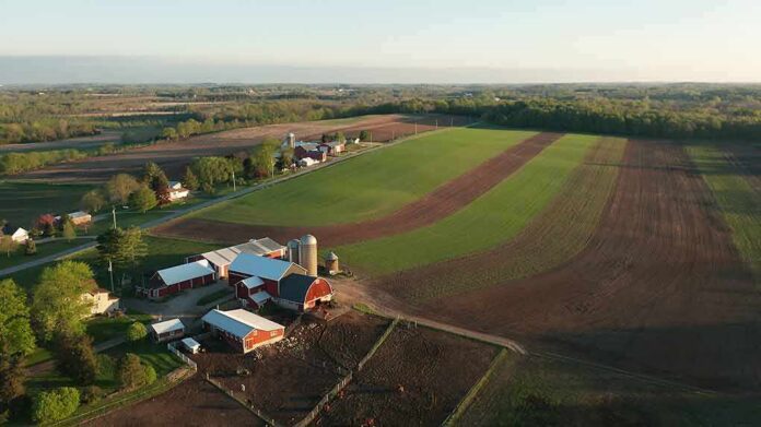 shutterstock_1737529889 Aerial view of a farm with red barns and expansive green and brown fields