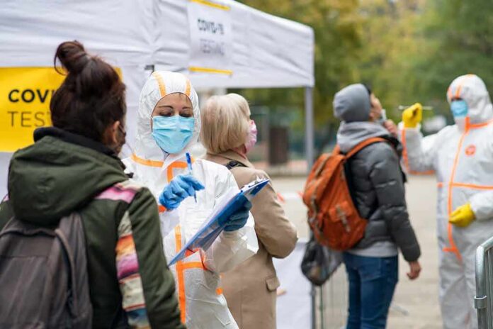 shutterstock_1850331961 Healthcare workers in PPE assist people at an outdoor COVID-19 testing site