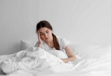 How Poor Sleep Worsens Chronic Pain Woman sitting in bed looking tired with hand on head