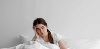 Woman sitting in bed looking tired with hand on head